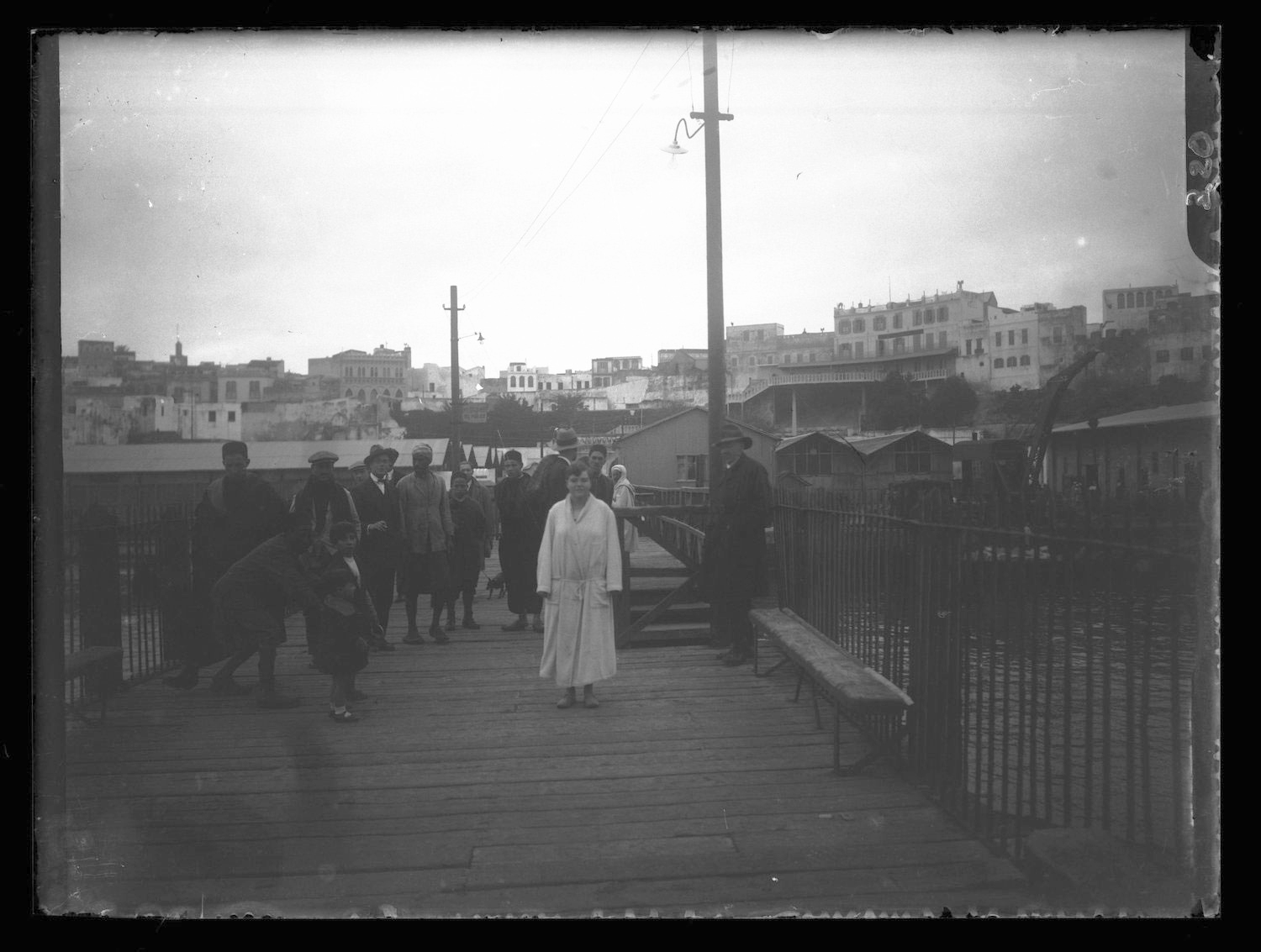 Millie Hudson (or possibly Mercedes Gleitze) in a robe on the quai, with the city in the background