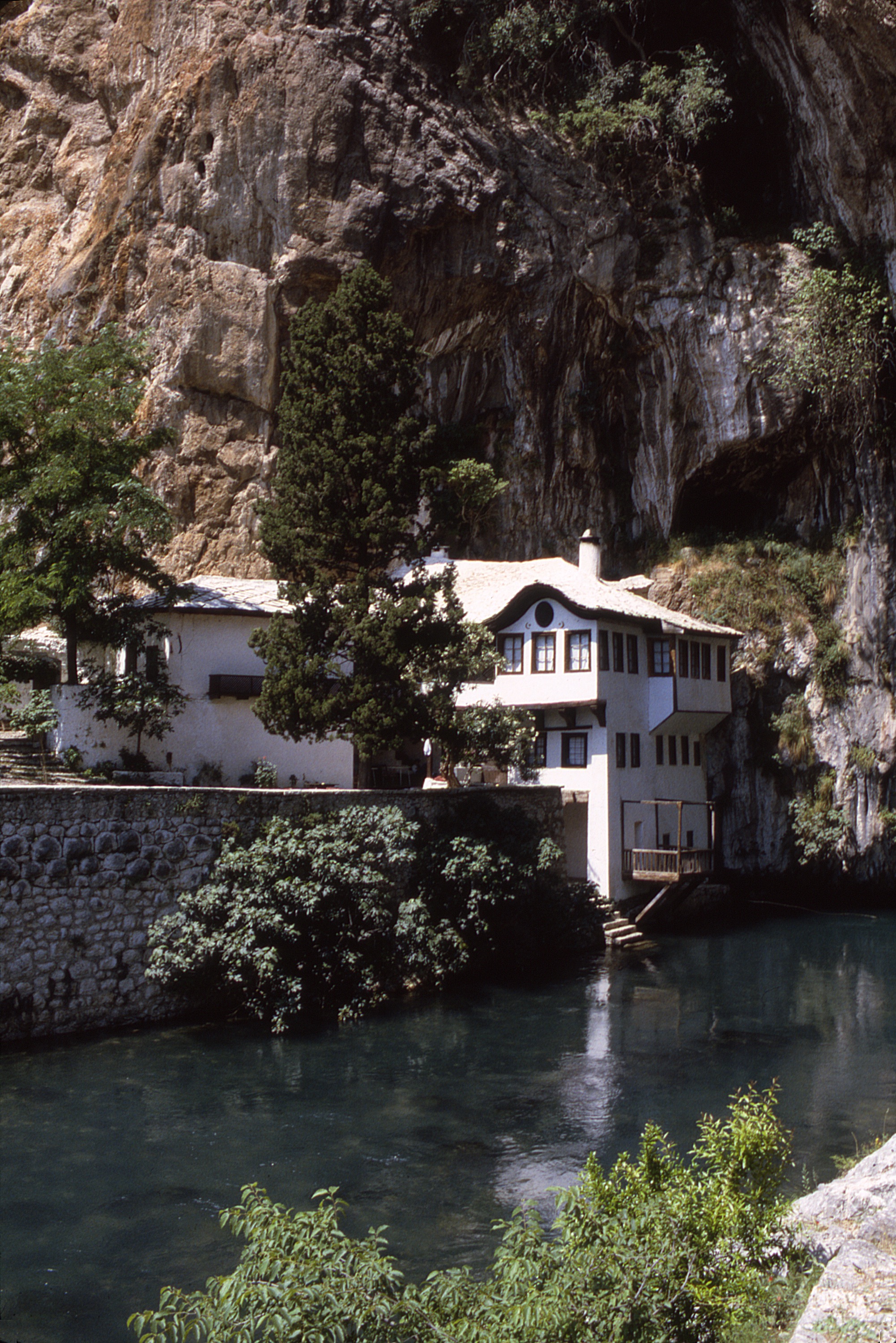 <p>The village of Blagaj na Buni is located southeast of Mostar in the Neretva Canton of Herzegovina. The Buna River emerges from under the massive karst stone formation after traveling over 19 kilometers underground. Archaeological finds indicate that the area has been inhabited for over 5,000 years. The present tekija (dervish monastic complex) dates back over 300 years. The karst formation extends high above the tekija to sites where ruins of fortresses occupied by Illyrians, Romans, and medieval rulers are located.</p><p>(photo 1988)</p>