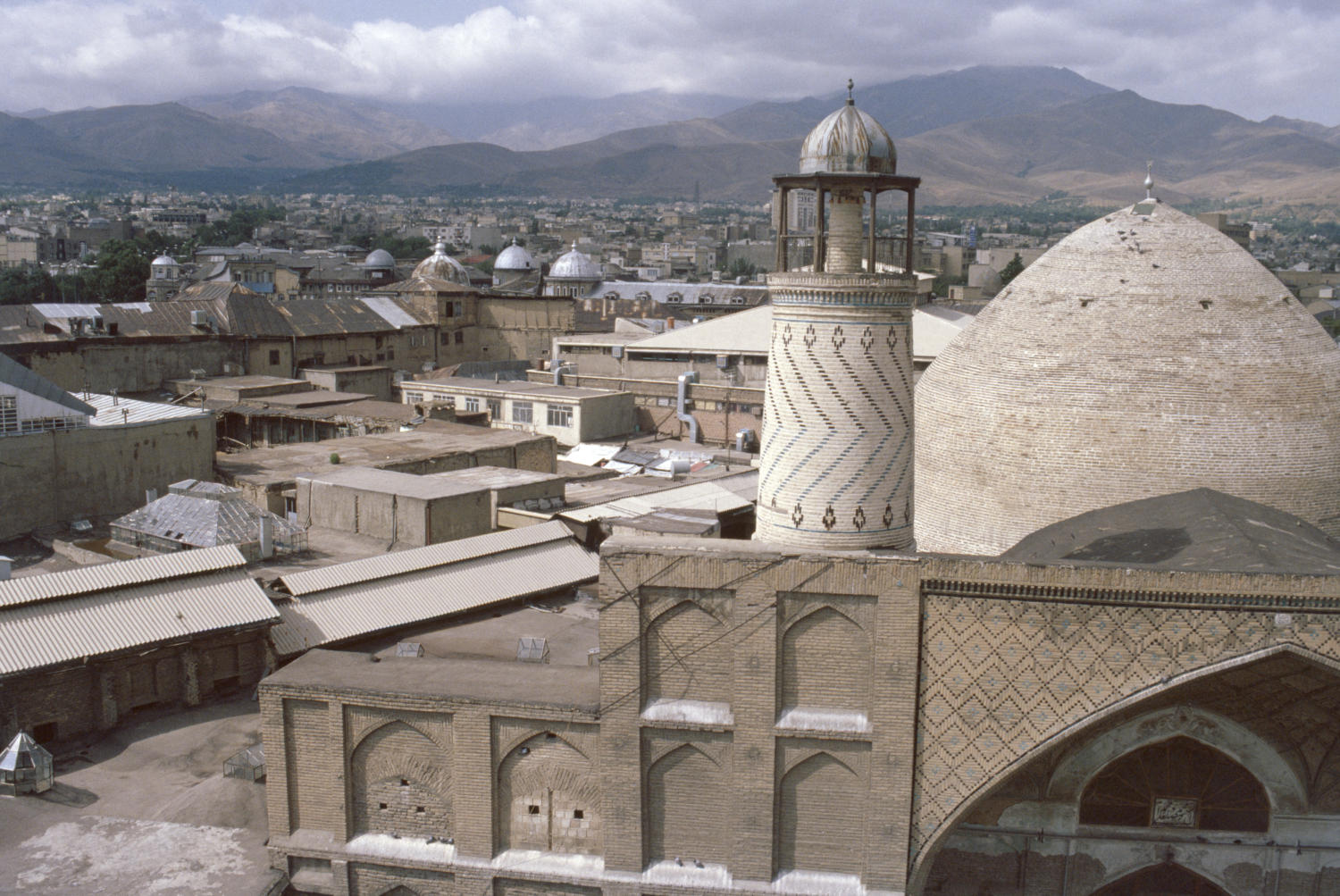 View of dome and minaret of qibla iwan seen from opposite rooftop. The bazaar of Hamadan is visible in the background.