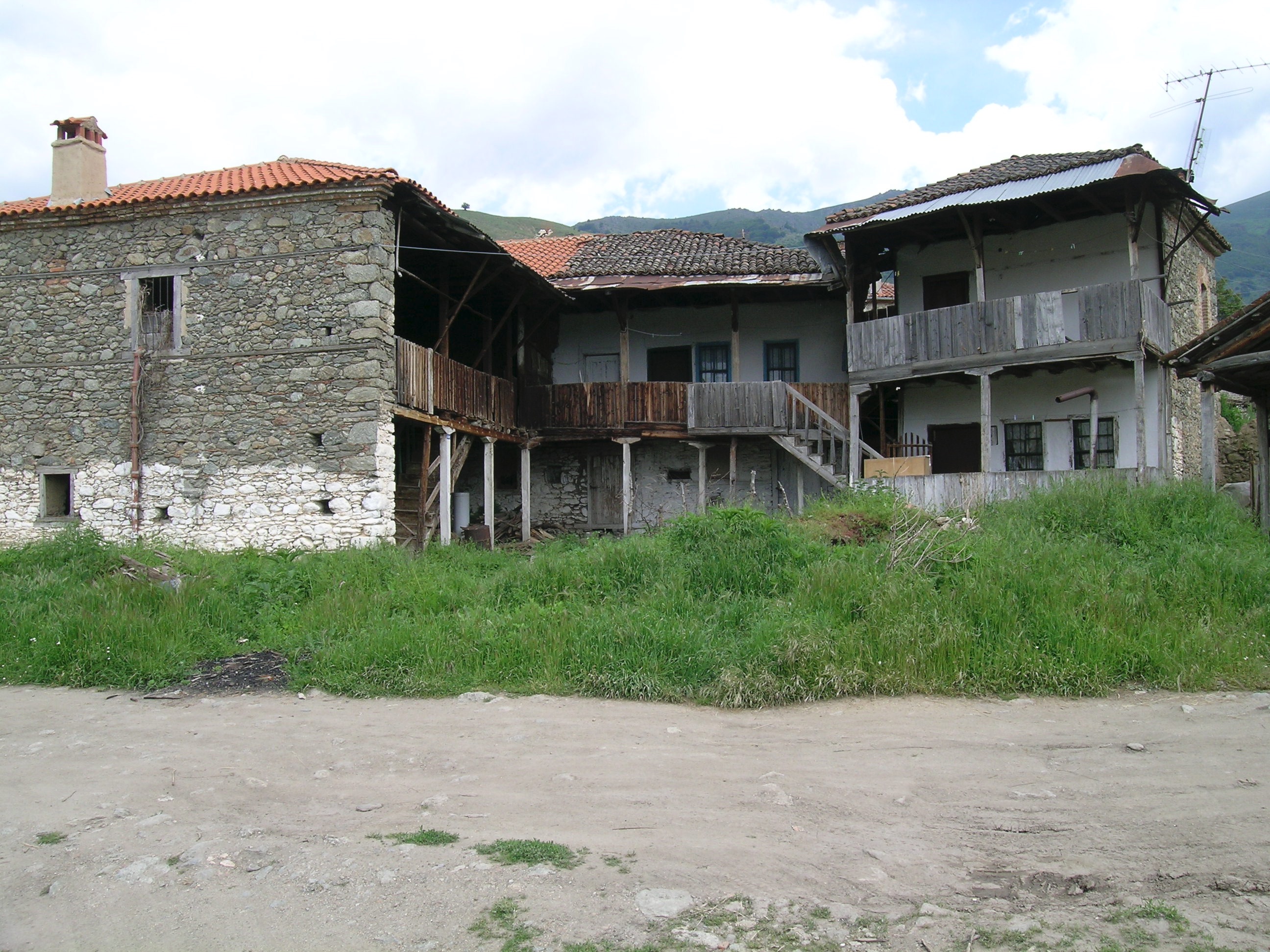 <p>In this complex of three dwellings, each structure has its own porch (tsardaki) element. The structure on the left has a new roof and chimney with its own exterior stair leading up to the tsardaki above and diagonal brackets to support the extended roof. The structure in the rear appears to join the other two structures together by modifications to the porches and a stair to link it to the structure on the right.</p>