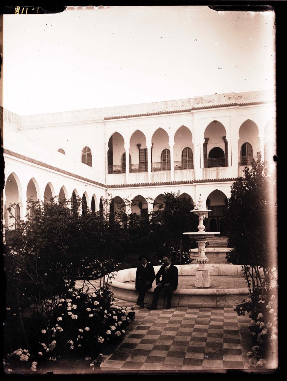View of two people at the fountain in the courtyard of a large house, possibly Moulay Hafid's Palace