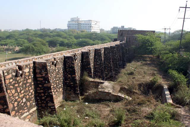 Exterior view of the Satpula dam from the western bastion, showing the buttresses and the elevated walkway. The raised ground to the south created by silt build up can be seen at right