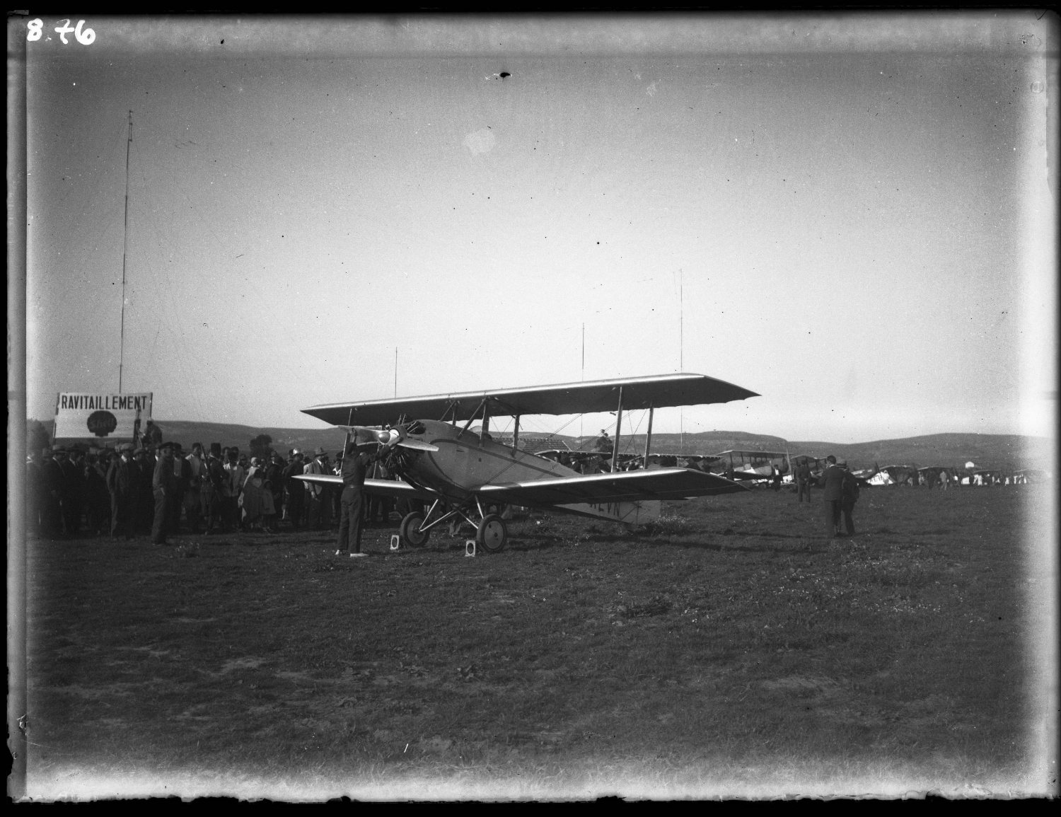 Side view, plane preparing for take off at airfield, crowd in European dress observing as a man services propeller