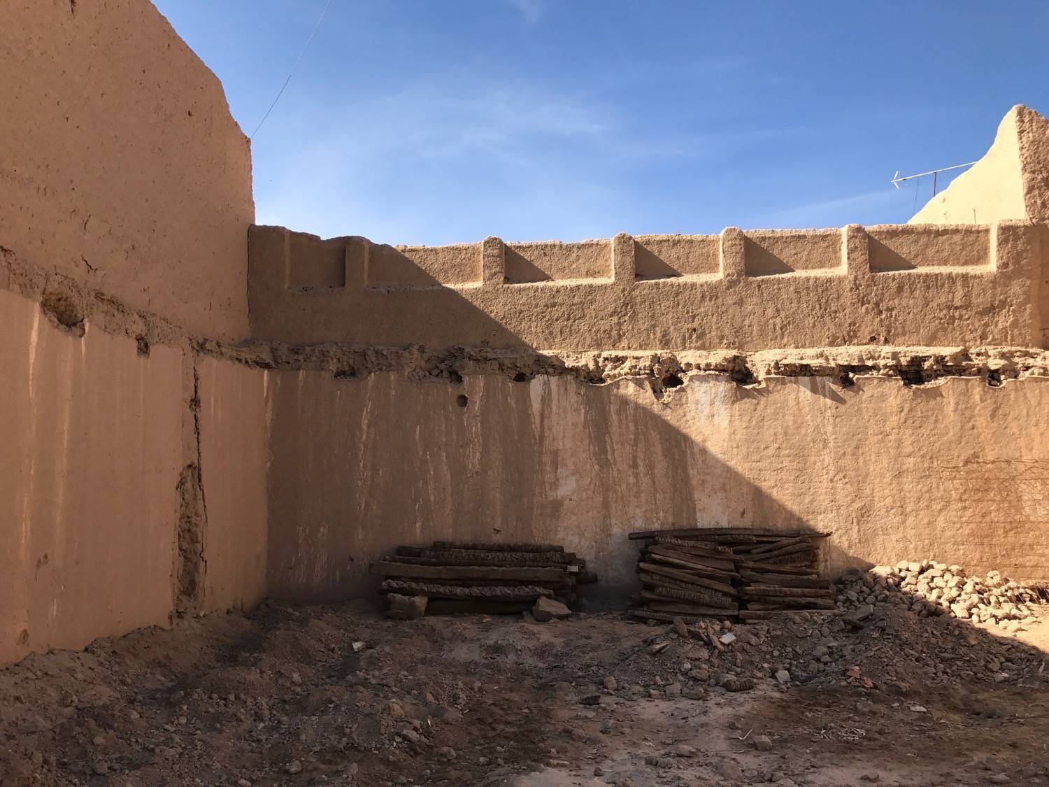 Ksar Rissani - Palm tree trunks used in various aspects of construction are stacked against a wall that is to be repaired  