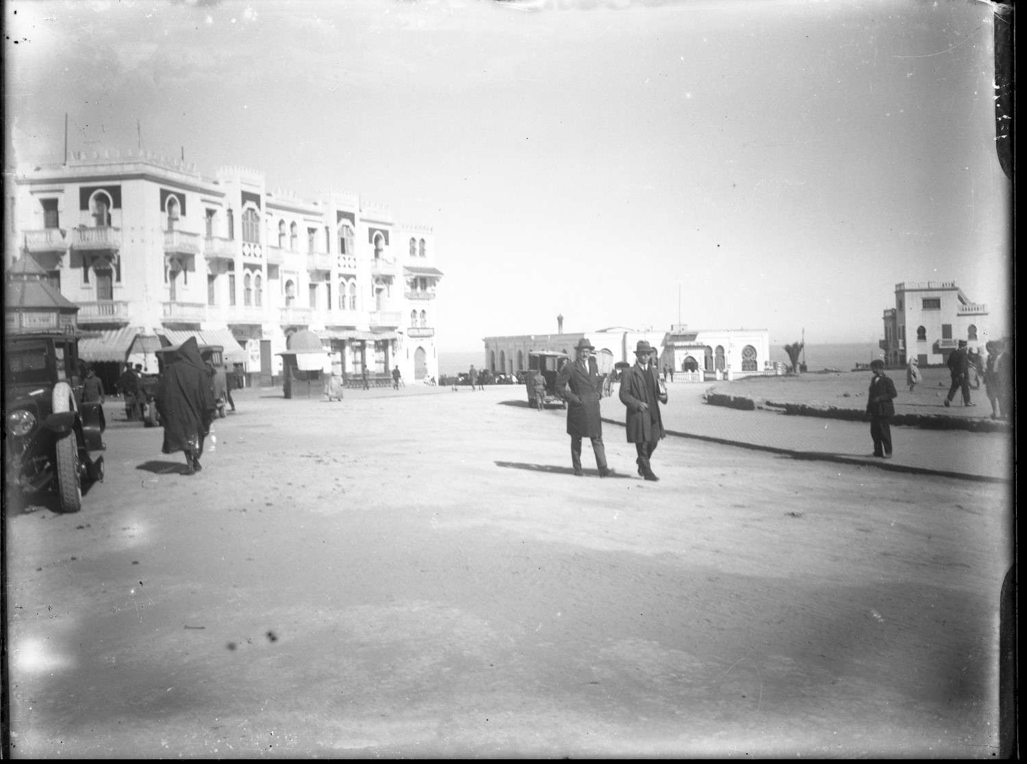 People in European and traditional dress walking in the Place de la Liberation, with the Oued Loukos in the background.
