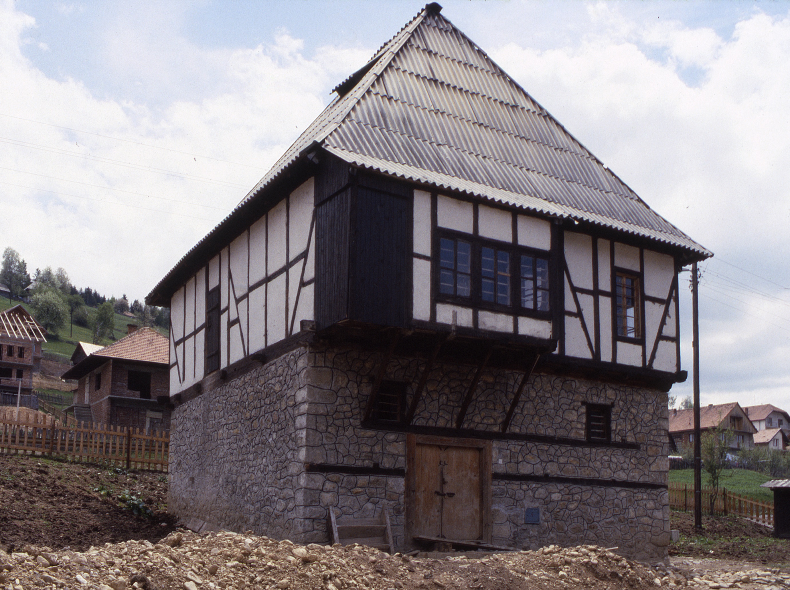 <p>This traditional kuća is undergoing renovations. The lower level walls are constructed of stone with integrated wooden reinforcing strips to stabilize the walls and provide lintels over doors and windows. The upper level floor, walls, and roof are timber framed. The walls were constructed using wattle and daub infill with a plaster coating. The roofing appears to be made of cementitious corrugated panels. The steep hipped roof is traditionally covered with wooden shingles (šindra) and has venting strips in the upper portion of the roof.</p>