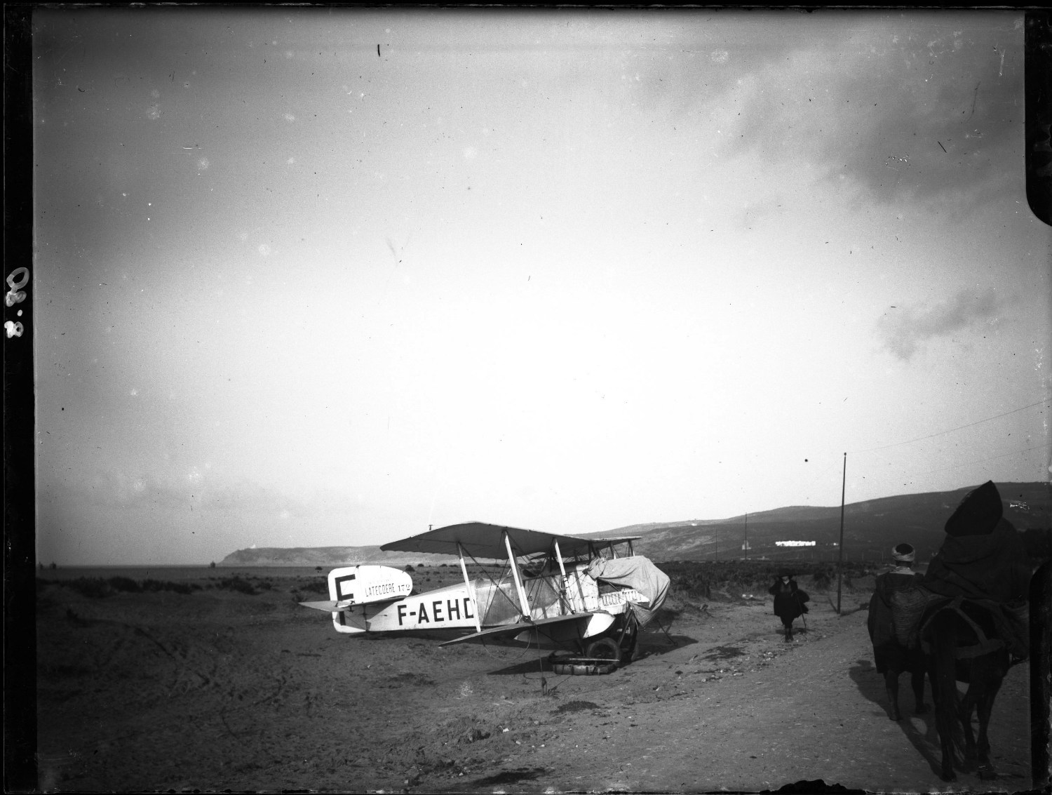 Side view of small white plane under tarp, men on horseback and walking in Moroccan dress