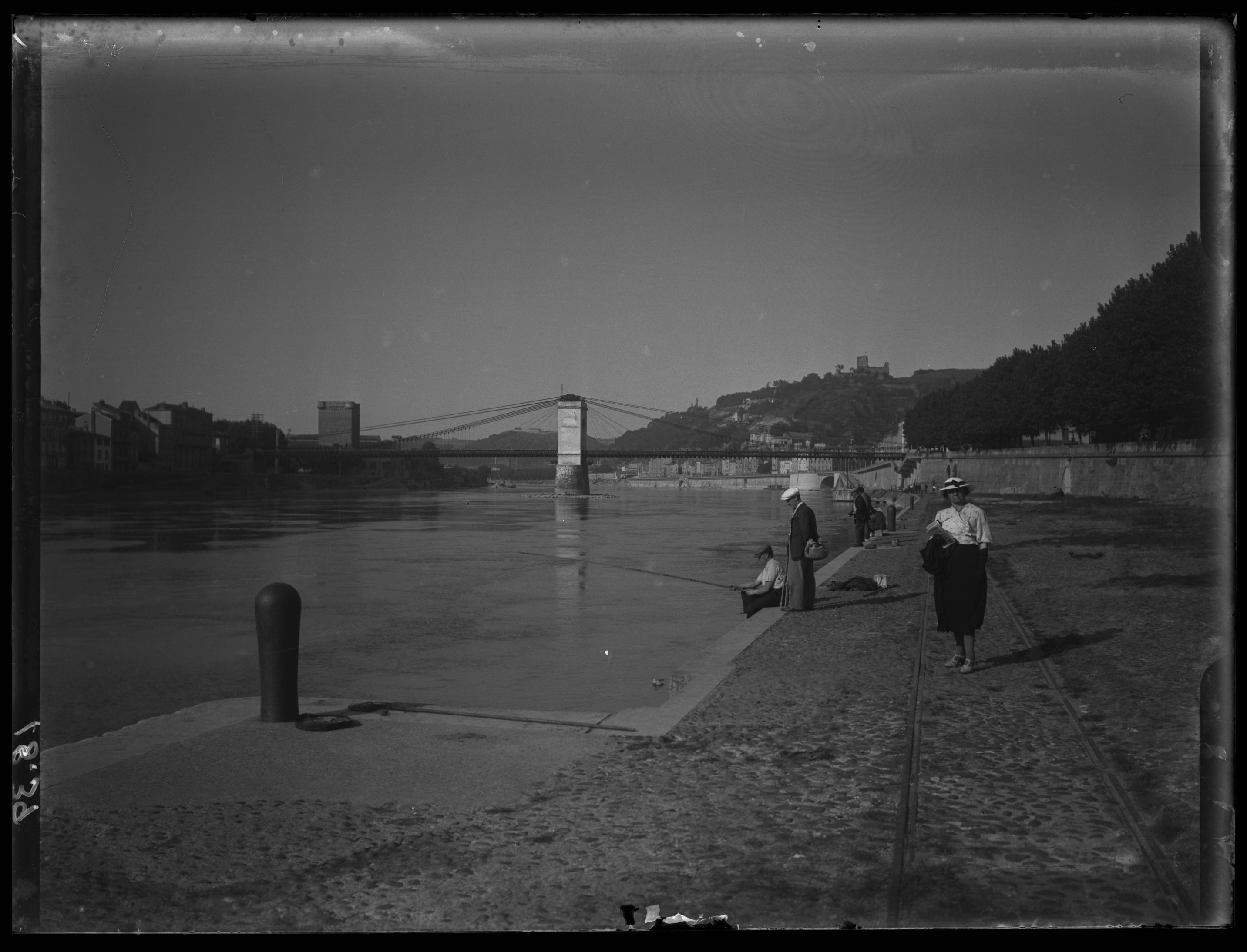 Paul Servant - <p>People in European dress walking and fishing by river, bridge in background</p>
