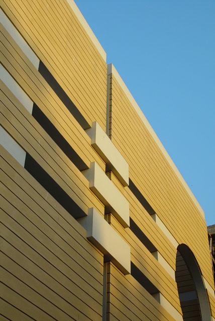 Detailed view of the facade, with tinted colourcrete finish, plastered to create a rythm of horizontal lines alternated with a smooth white plastered finish on the columns and pilotis