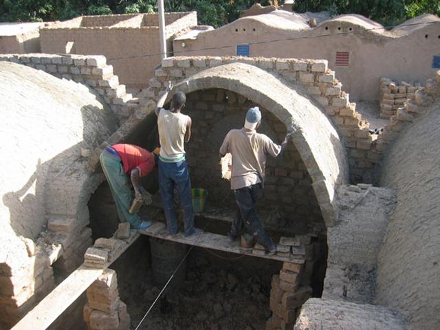 Workers starting the building of a vault. Completed vaults are visible at the rear. Boromo, Burkina Faso