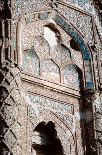 Gunbad-i Qabud - Exterior detail of entry elevation, showing a typical arch tympanum carved with three-tier muqarnas and framed by inscription band in blue tiles. The surfaces of tympanums and spandrels of exterior arches are decorated with glazed and unglazed terracotta in intricate geometric patterns