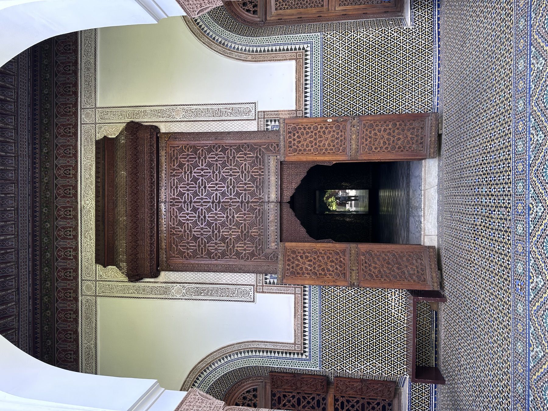 <p>View to a portal with carved wood doors, frame with carved stucco, zellij flooring, and painted wood ceiling</p>