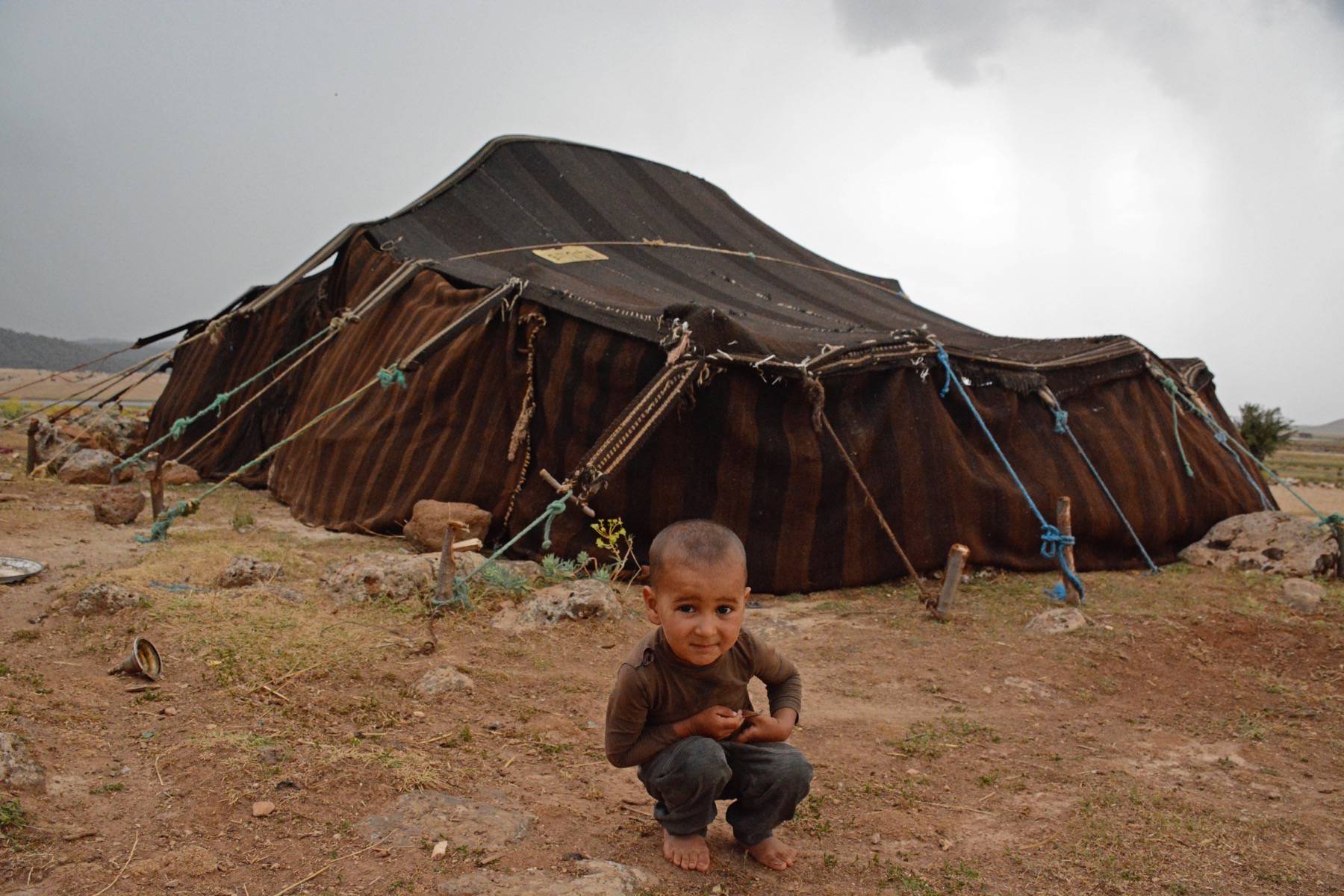 Small boy in front of Amazigh (Shilha) tent (handwoven fabric, cotton and wool, rope, wooden stakes), Lake Efnorir, Ain Leuh, Azrou, Middle Atlas Mountains.