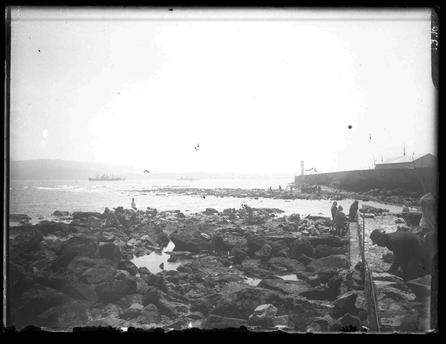 View across the rocky shore toward the wall of the quay of the port during construction