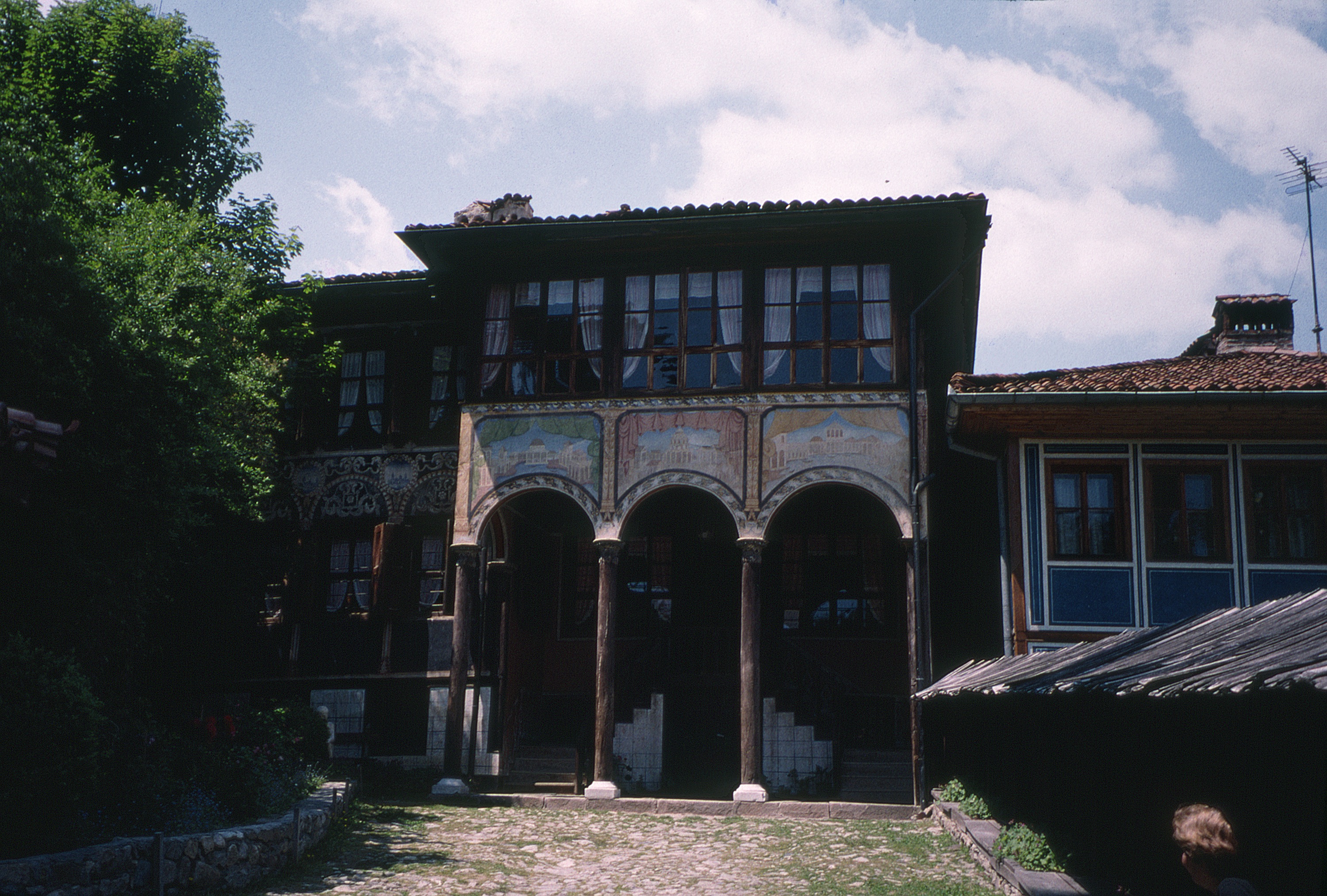 <p>The Oslekova kăšta, constructed in the 1850s, represents the late national revival period of traditional dwelling architecture. Koprivštica had become a wealthy town and a center of resistance to the Ottoman powers. The dwelling was conceived as a symetrically organized composition but Nenčo Oslekov was not able to purchase the property to the right. The grand dwellings of this period replaced the čardak space with a central salon with glazed openings on each level. The building design is attributed to Usta Minčo and murals by Kosta Zograf, both artisans from Samokov.</p>