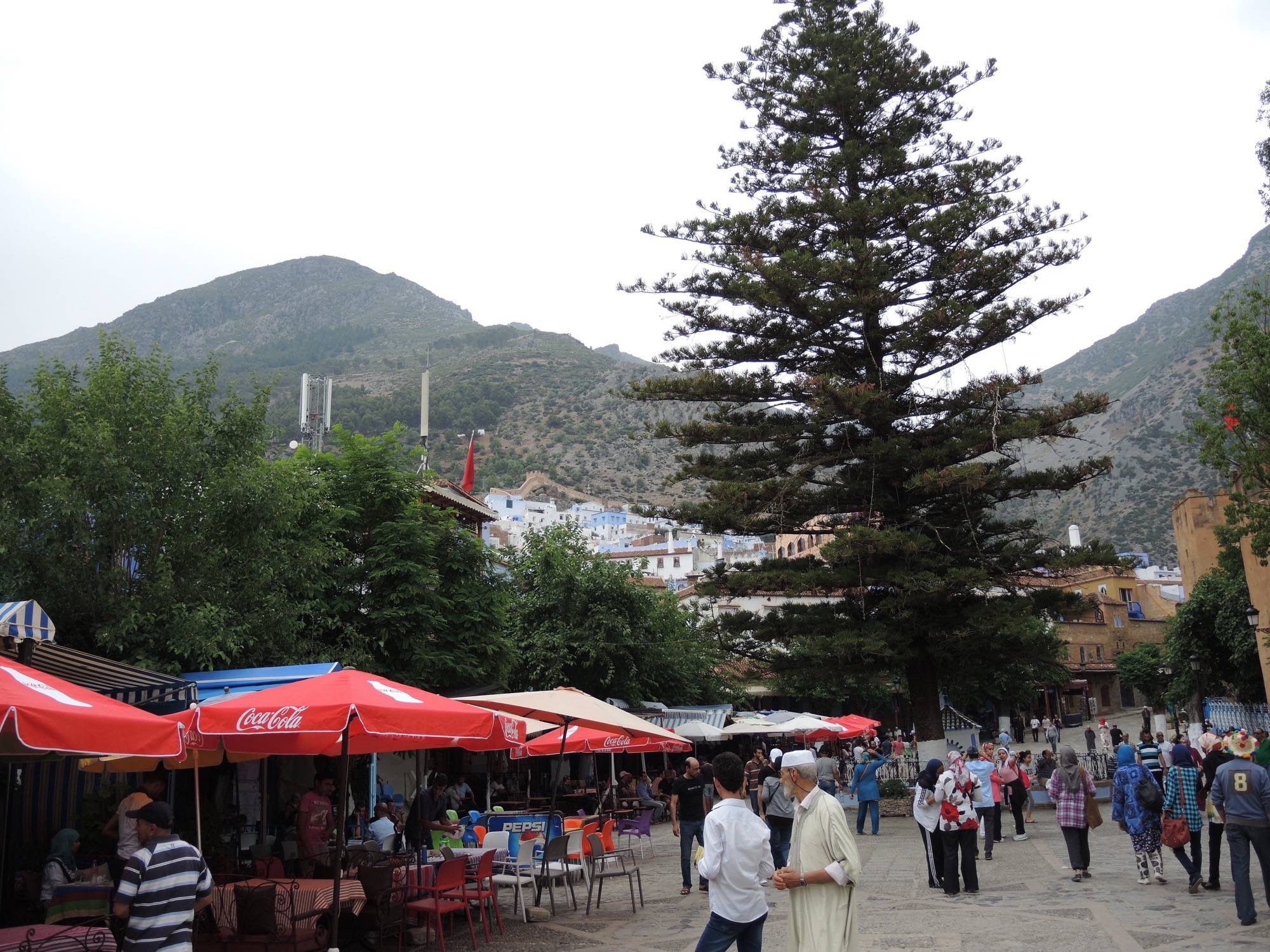 General view of the square from the medina toward a mountain.  The casbah tower is on the right.  A section of the city walls is visible in the background of the photograph.