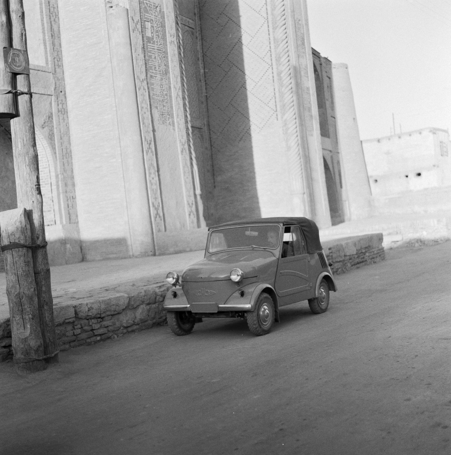 A car on a road in front of Madrasah-i Ulug Beg.