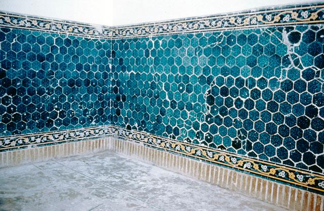 Interior view showing dado of hexagonal blue tiles bordered by tile mosaic bands with floral motifs