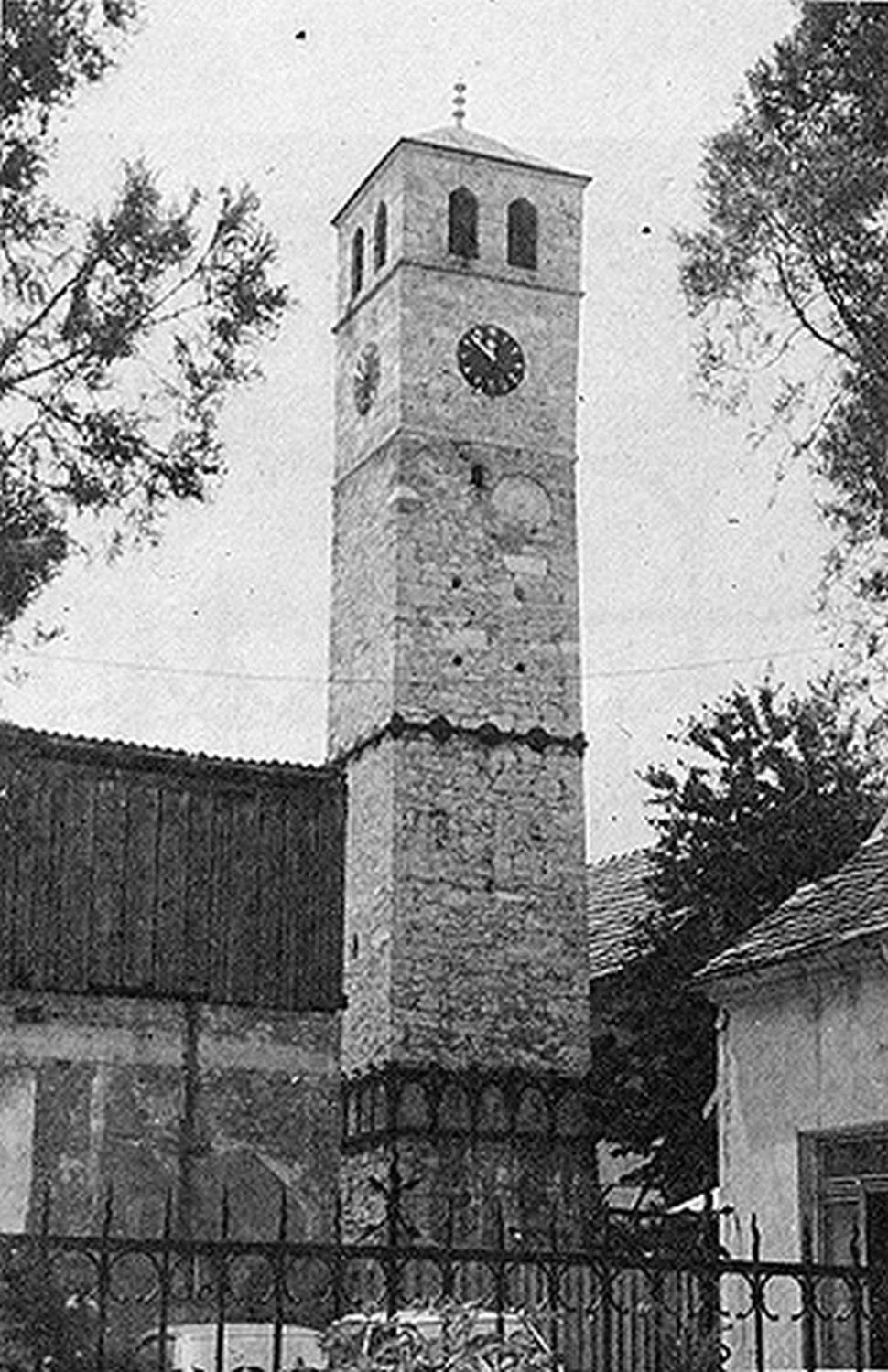 View of the clock tower (sahat kula) of Ferhad Pasha Sokolovic, when it was still standing across the street, on the west side of the mosque complex facing Ferhad Pasha's mausoleum (turbe). The clock tower was built as an Islamic endowment (waqf) by Ferhad Pasha Sokolovic in the 16th century.  Ferhad Pasha's clock tower was blown up on December 15, 1993, seven months after the Ferhadija mosque was blown up and razed.  It has not been rebuilt as of 2016.