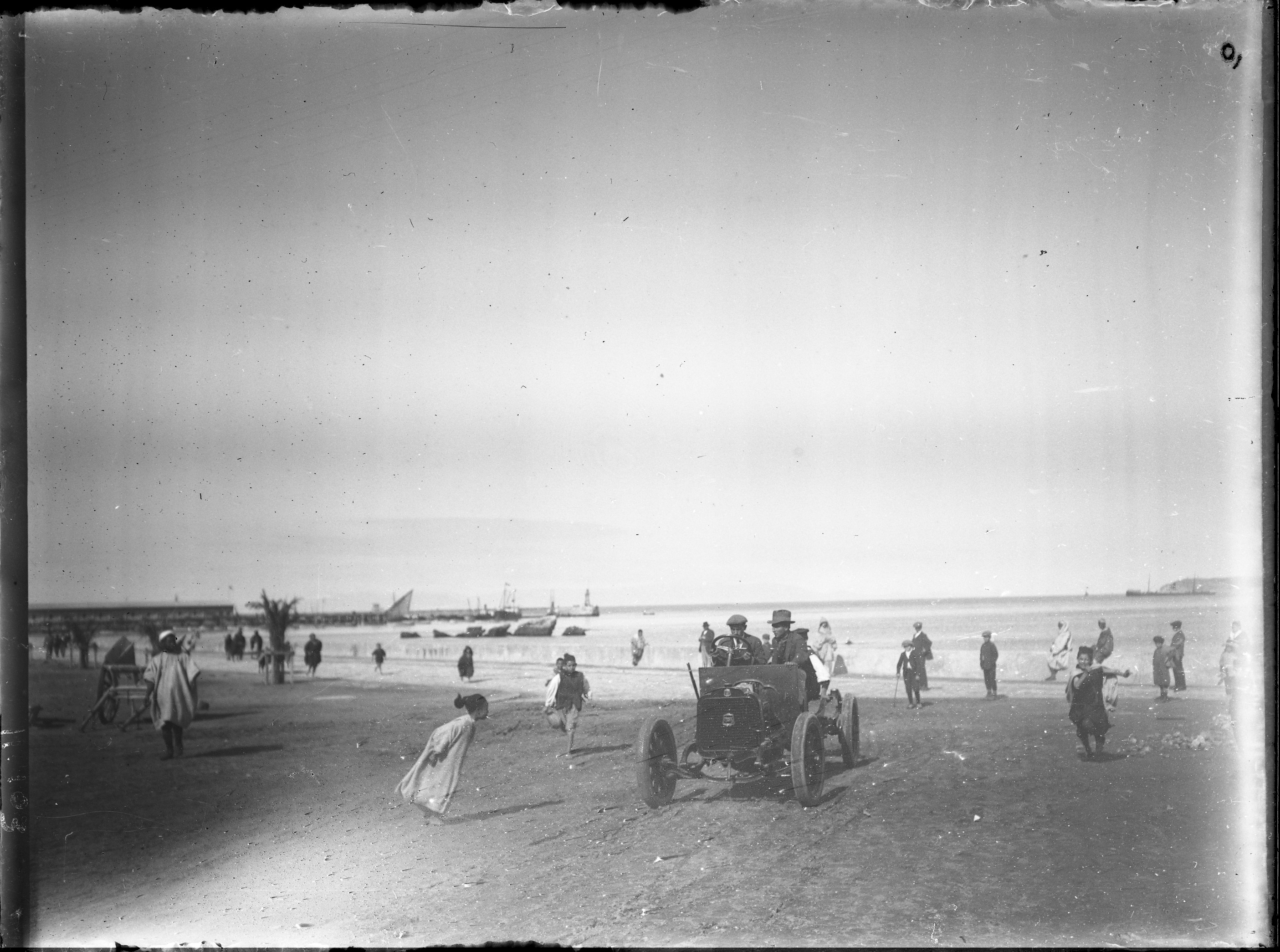 Port (Tangier) - <p>View toward the port of Tangier of two men driving a car among children playing on the beach</p>
