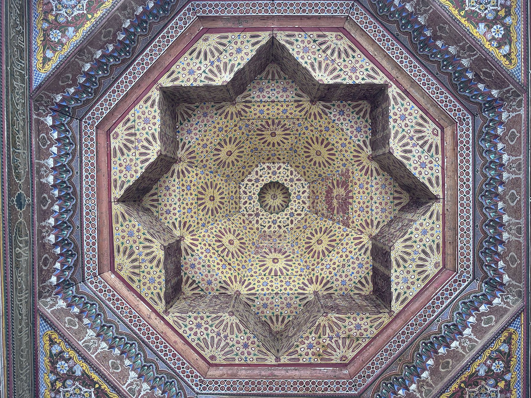 <p>View of an octagram ceiling recess in a painted wood, octagonal frame, decorated with geometric patterns, floral motifs and muqarnas</p>