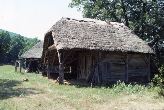 <p>The barn has an external structure with inboard enclosure plank walls. The straw roof appears to have an added light metal ridge cap. The rear of the roof has a full hip and the front a pent-hip form. Each of the wooden columns has braces to the head plate; the bases of the columns appear to rest on large stones. The wooden purlins accept the straw roofing material directly to allow for ventilation of the organic material.</p>