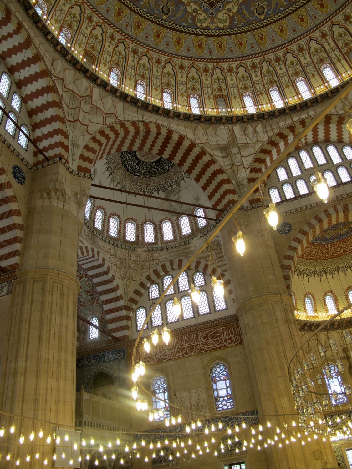 Interior view up and across prayer hall, showing part of the central dome, and some of the semi-domes and pillar.