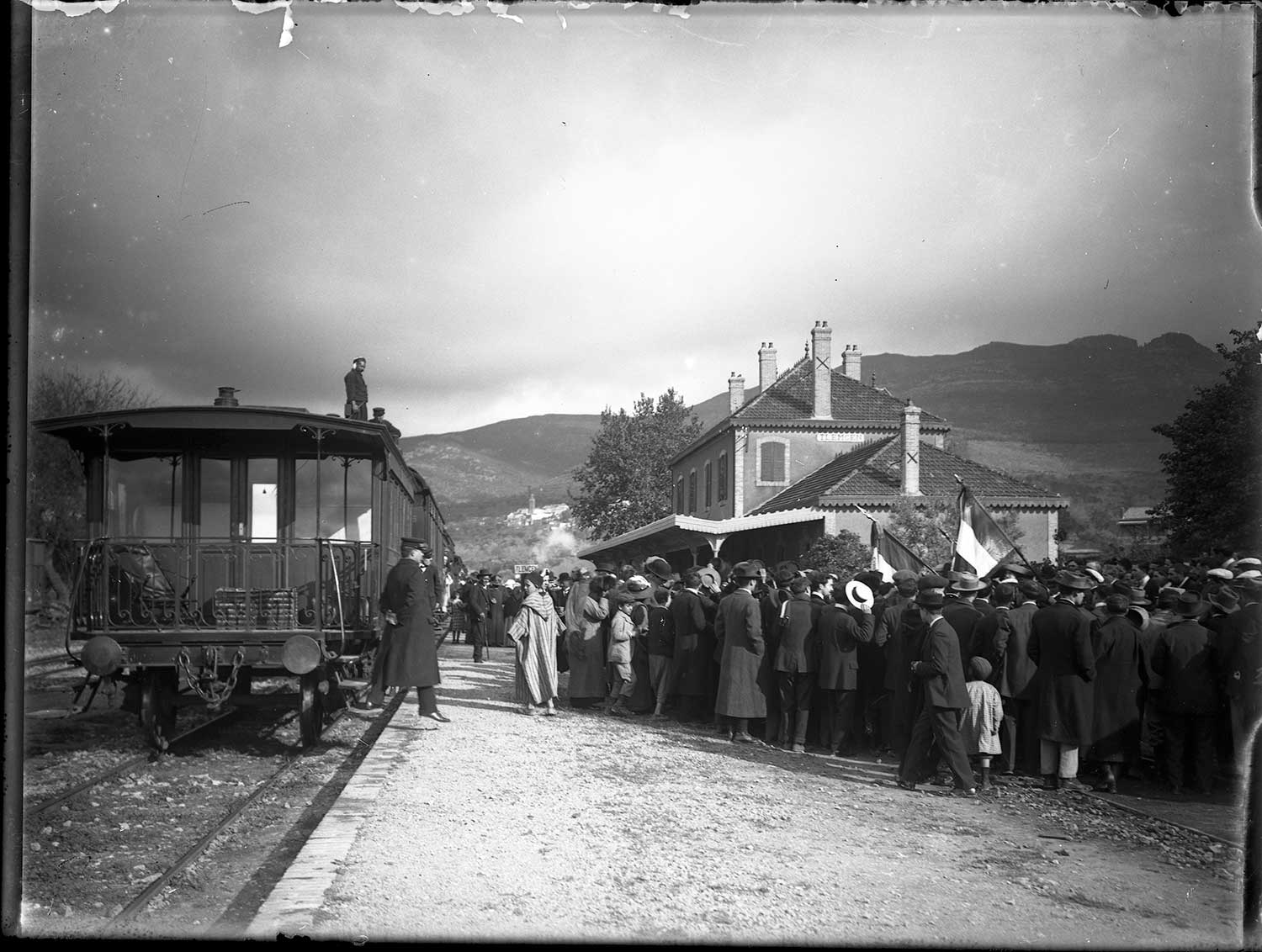 View of train and station house, with crowd waiting by the tracks