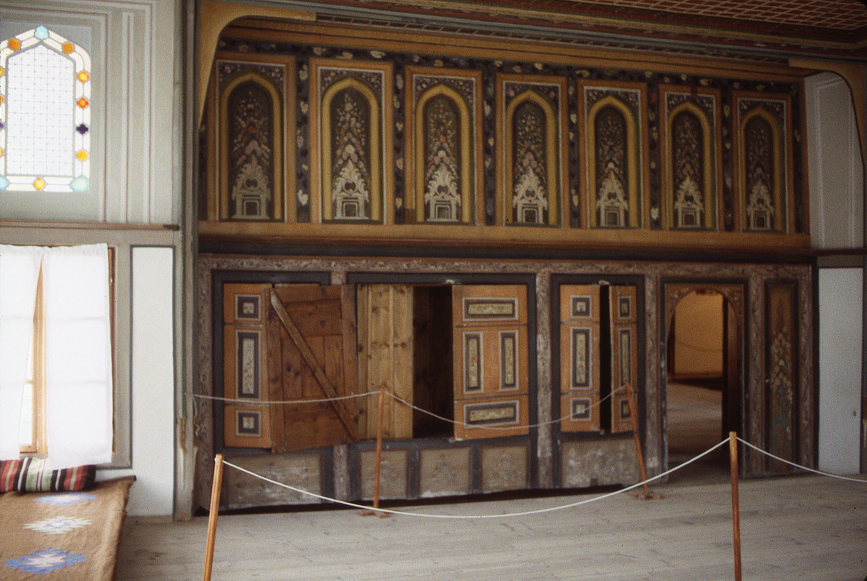<p>The large reception room in the house is known as the guest room (гостната стая) where guests and merchants were entertained during meetings. The paneled wooden cabinetry was made with a variety of woods and applied with decorative paintings; fixed wooden panels were installed above the projecting shelf. The room has windows on three of the exterior walls. The lower windows are transparent and operable while the upper windows are fixed and made with translucent and colored venetian glass.</p>