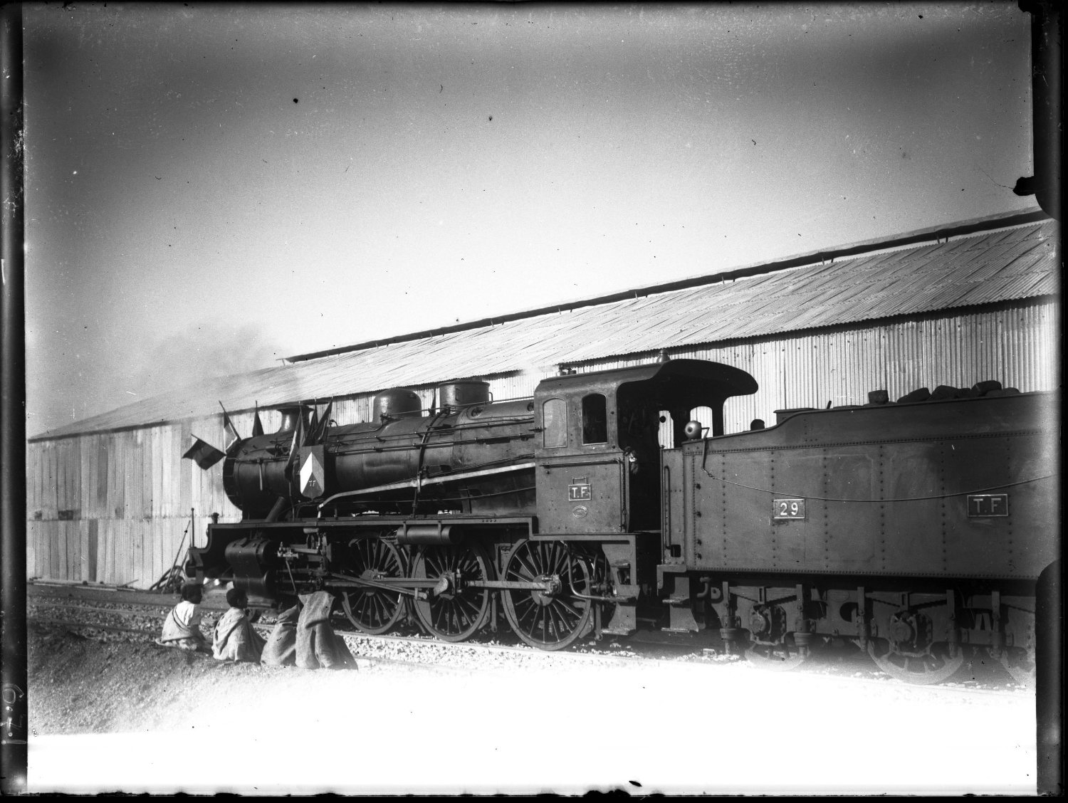 Side view of train in front of a building, four people in Moroccan dress sitting by the tracks