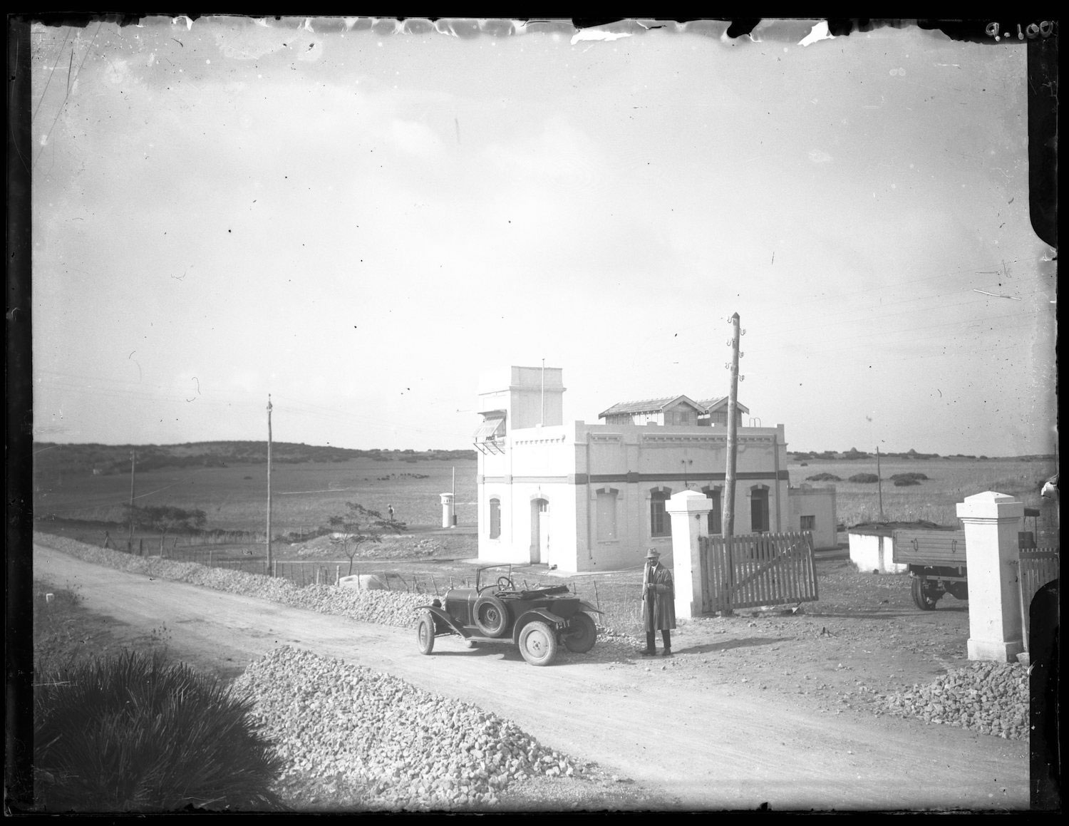 Portrait of man in European dress with car in front of a roadside structure