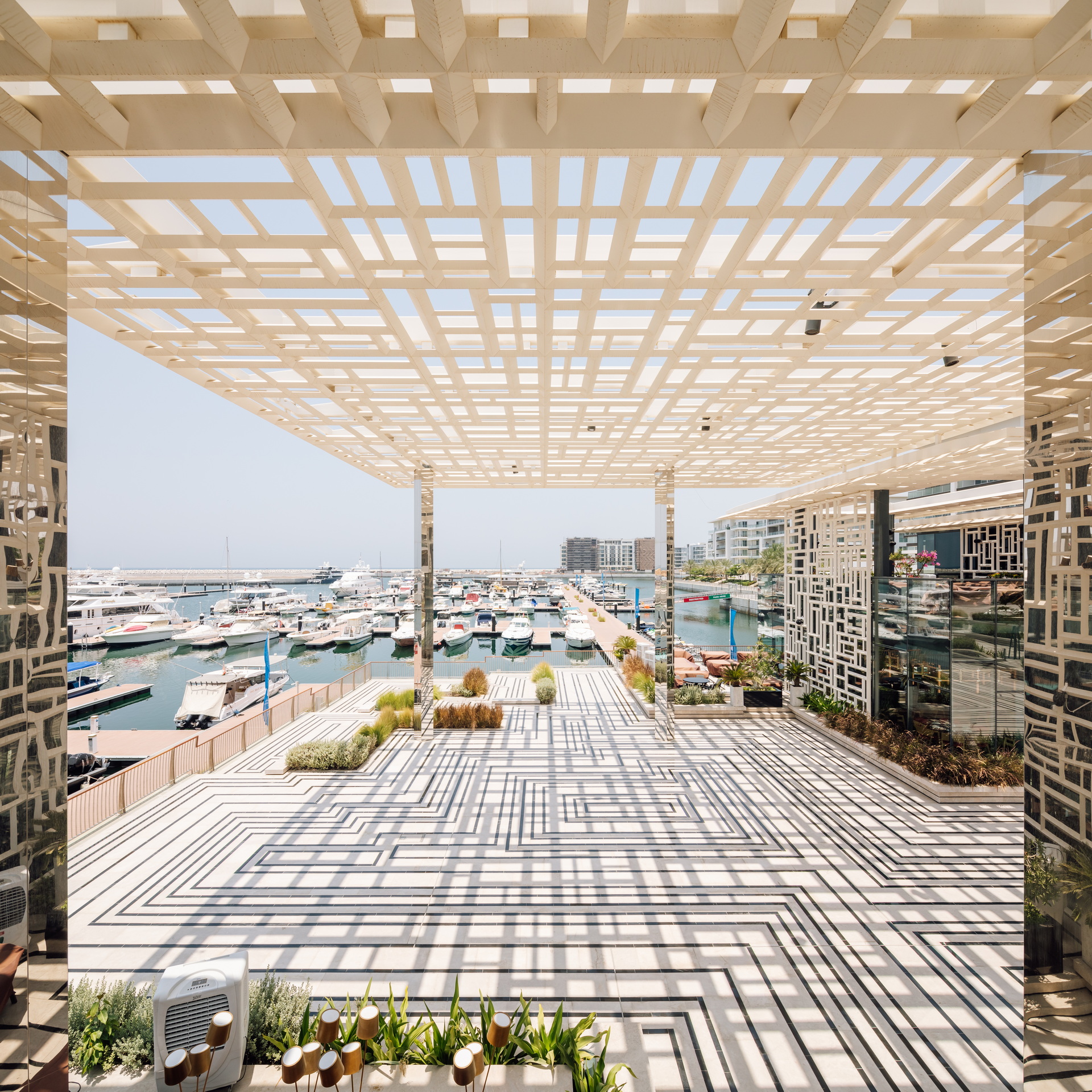 <p>The landscaped surface, of local Desert Rose marble inset with black granite lines, draws from traditional Omani patterns and shares a unified visual identity with the powder-coated aluminium mashrabiya walls of the restaurant and café buildings and the shading canopies, blurring the boundaries between elements.&nbsp;</p>