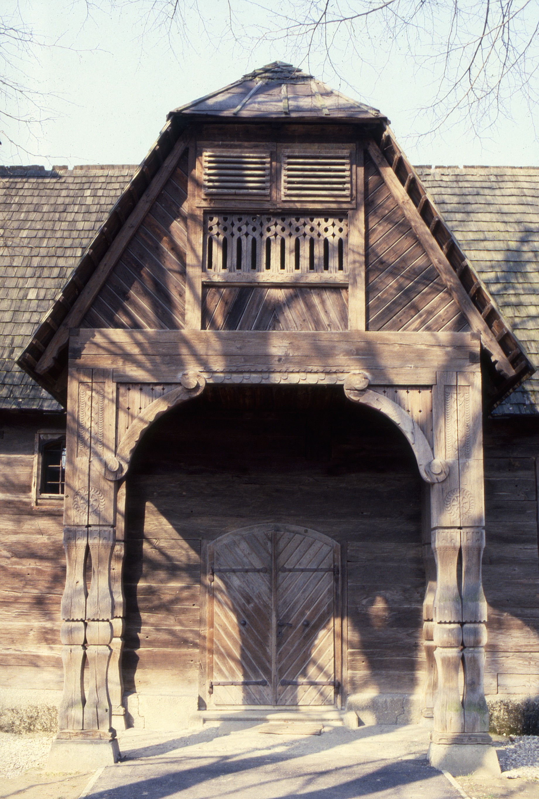 <p>The composition of shapes and woodworking within the upper framework (pediment) and subtlety of the carved details of the chapel's entry porch is evident in this sunlit view.</p>