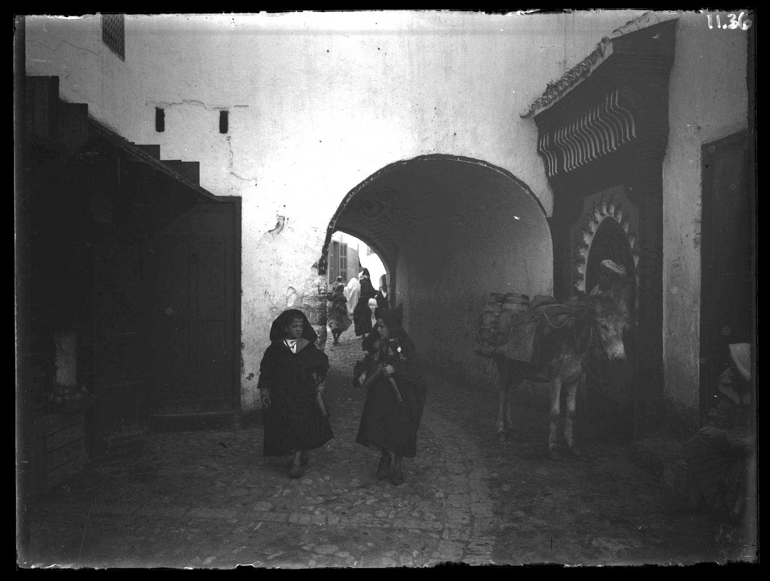 Two boys in cloaks walk through the gare; at right a donkey stands by the portal of Sidi Ali Ben Daoud