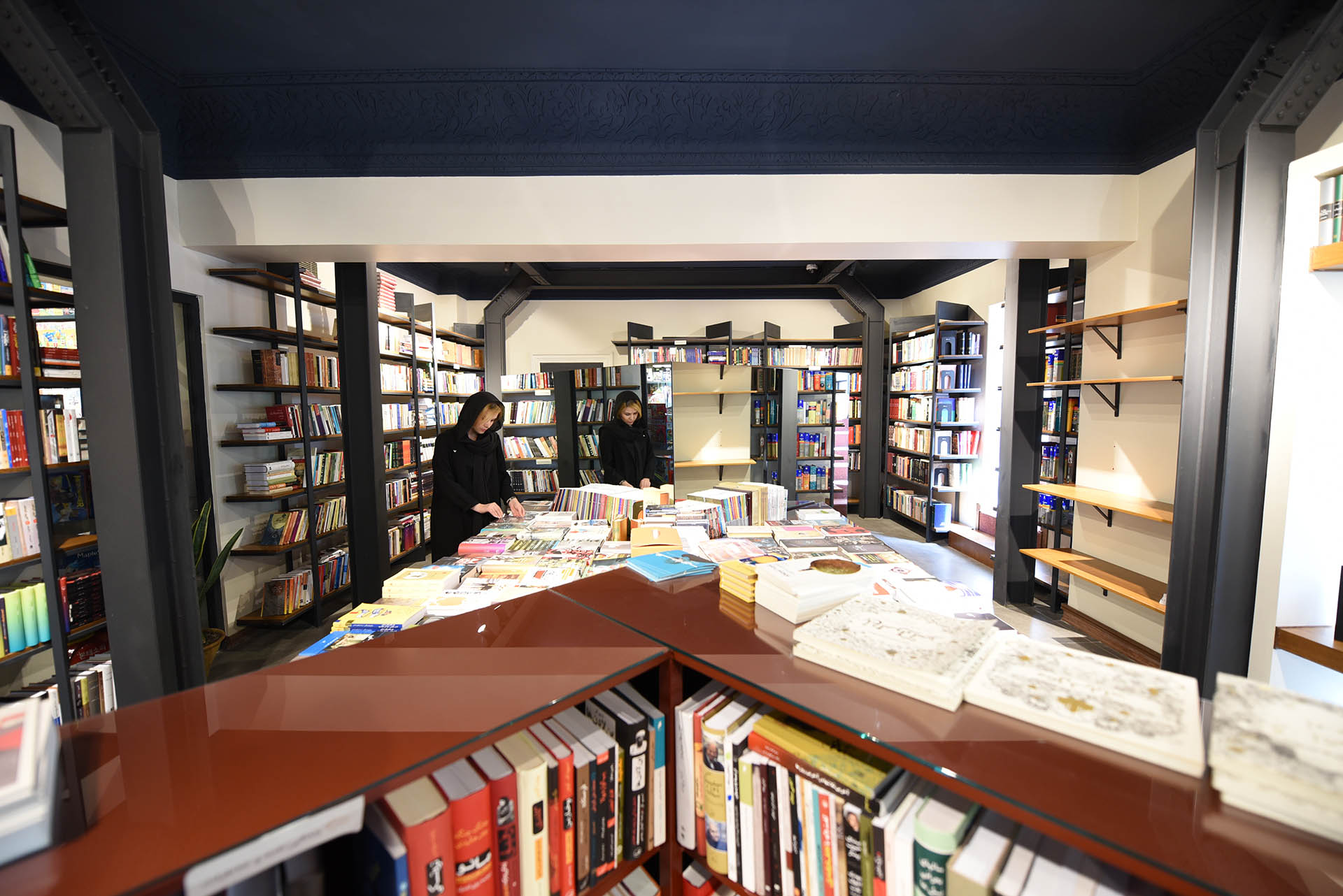 <p>Reflection of people on the mirror of book's shelves</p>