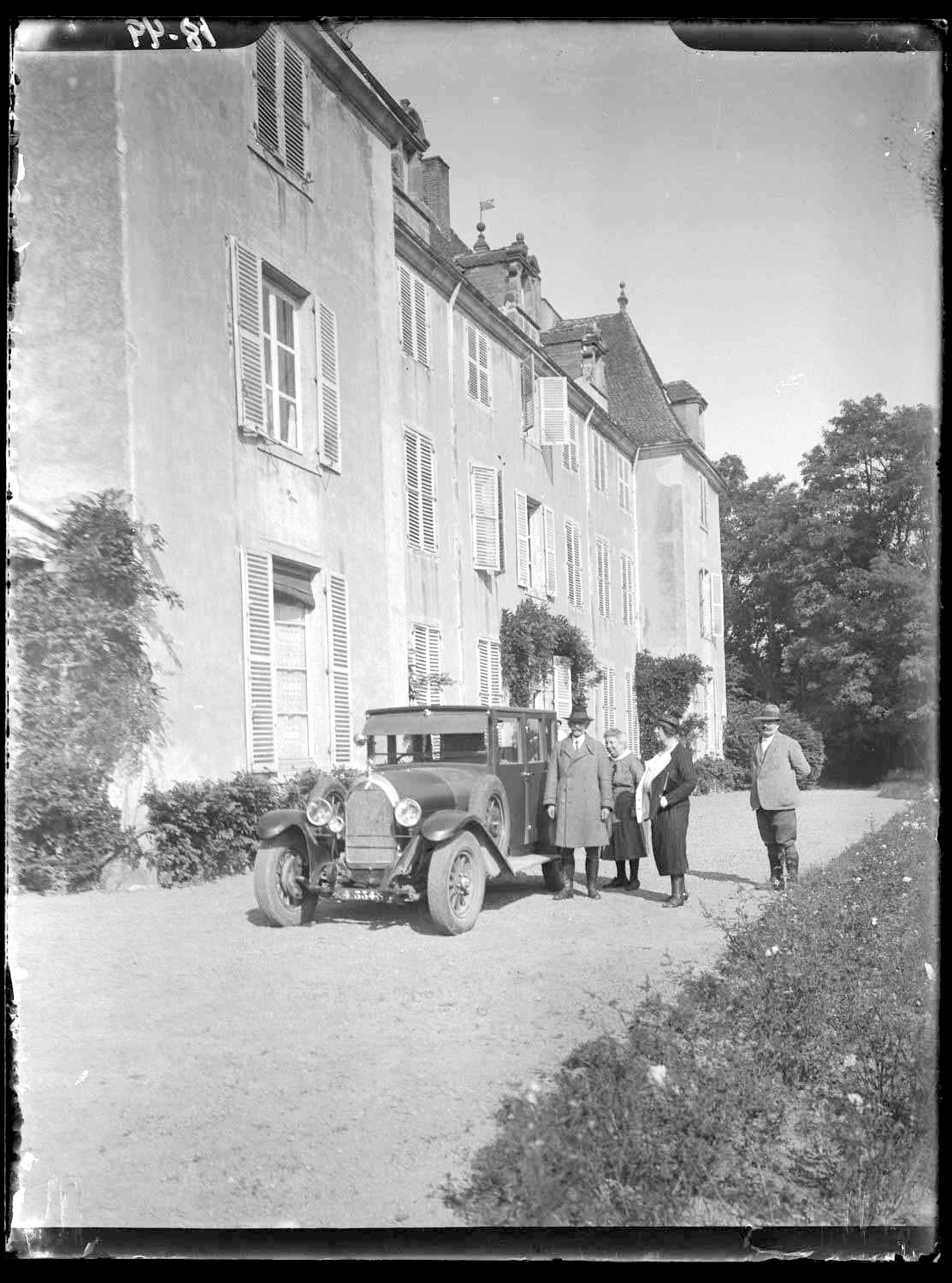 Paul Servant - Side view, group portrait of people in European dress by car in front of a residential building