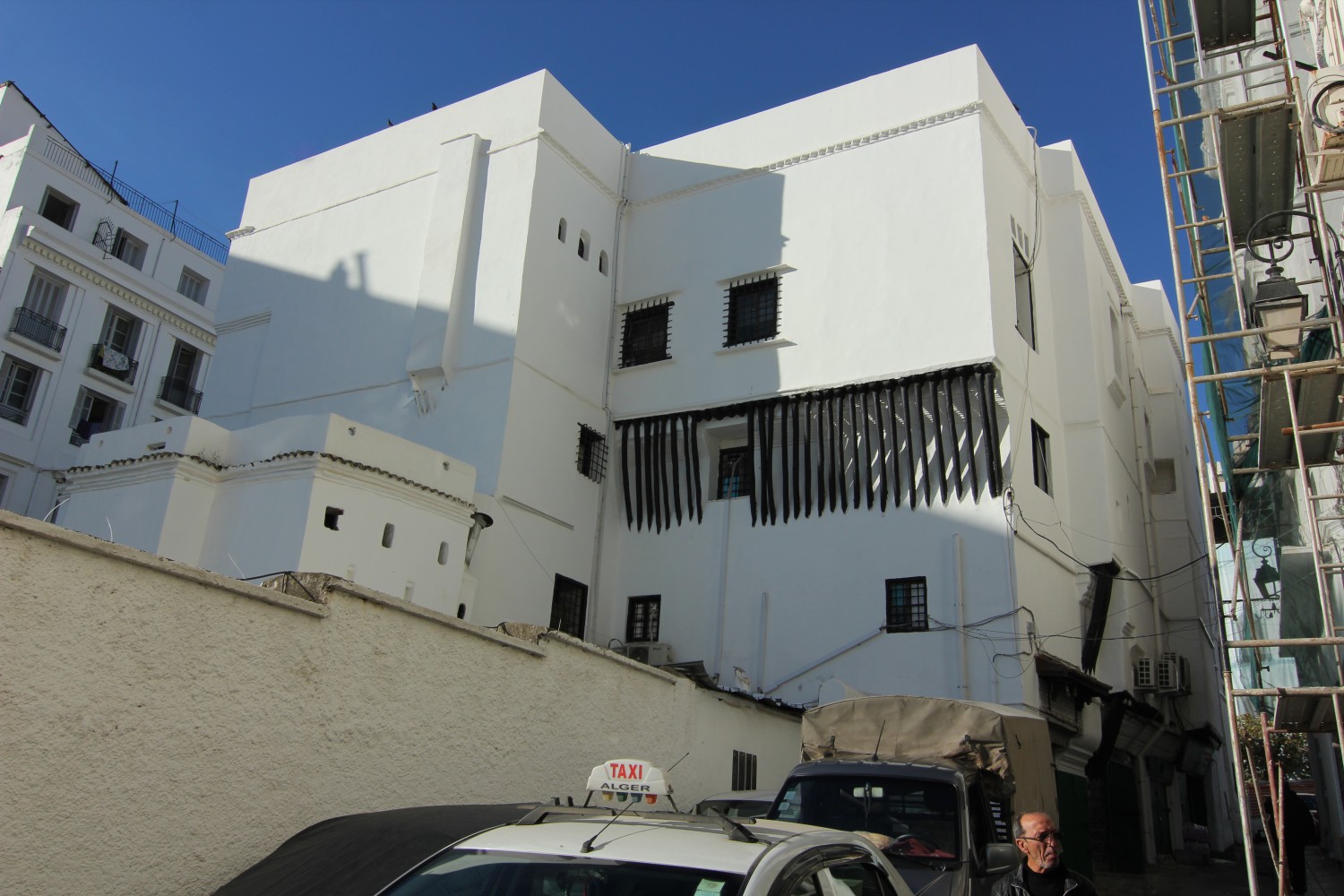 Rue Ben Ferhat, exterior view of Dar Aziza's east facade showing wood brackets, corbellings, dog-tooth cornices, and small windows with security bars