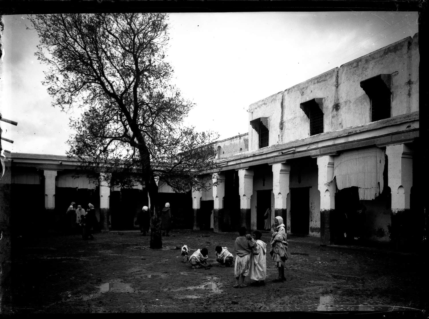 People in traditional dress in a courtyard with tree 