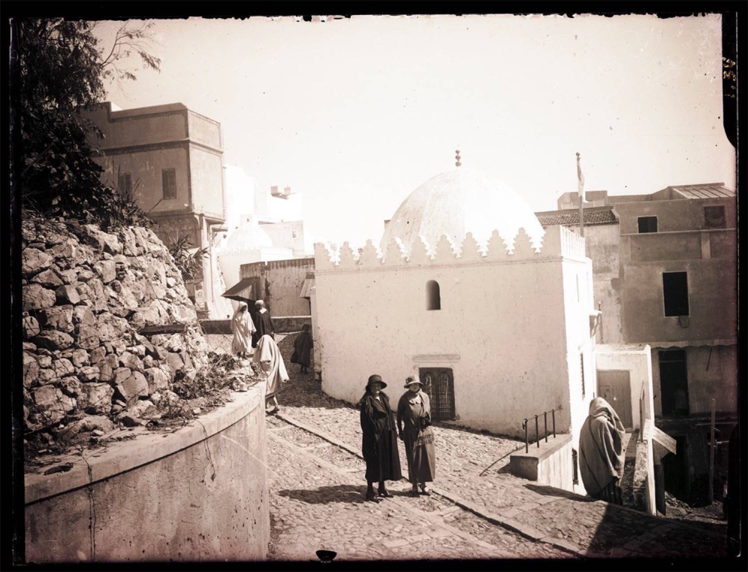 View of the Zawiya with two women in European clothing descending rue Ben Raissoul and a woman in Moroccan garb ascending the stairs from rue Sidi Hosni
