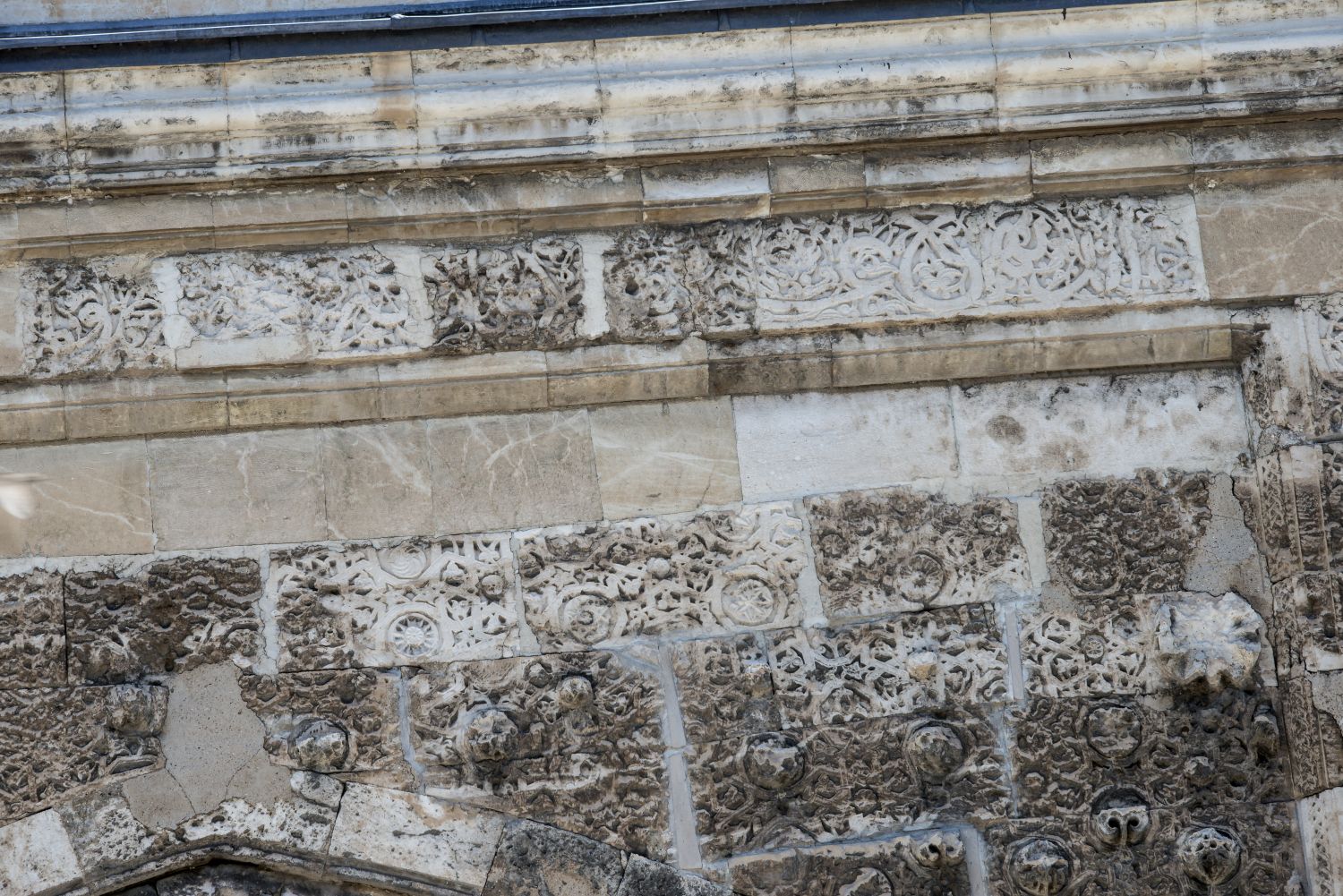 East iwan: detail view of upper portion of facade showing vegetal ornament within geometric frames carved on surface.