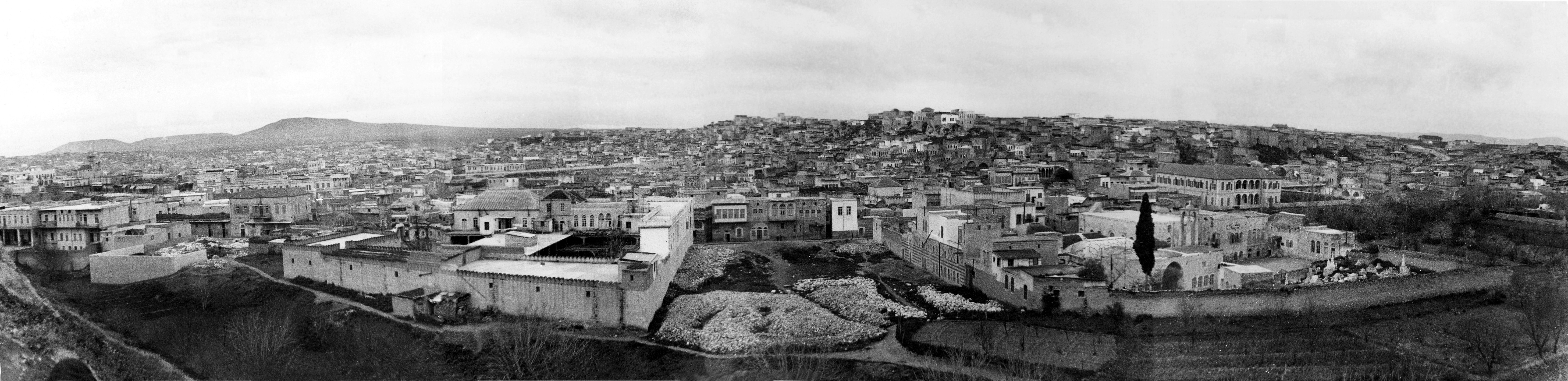  Hama - <p><strong>View from Hama Citadel towards Al-Madina Area</strong></p><p>Taken from Hama Citadel towards the southeast, this panorama showcases the Al-Madina area. Notable features include Al-Hassanin Mosque, with its minaret and dome to the left, and the Greek Orthodox church (Our Lady of Entry) to the right. In the background, the minaret of the Great Mosque is visible to the right.</p>