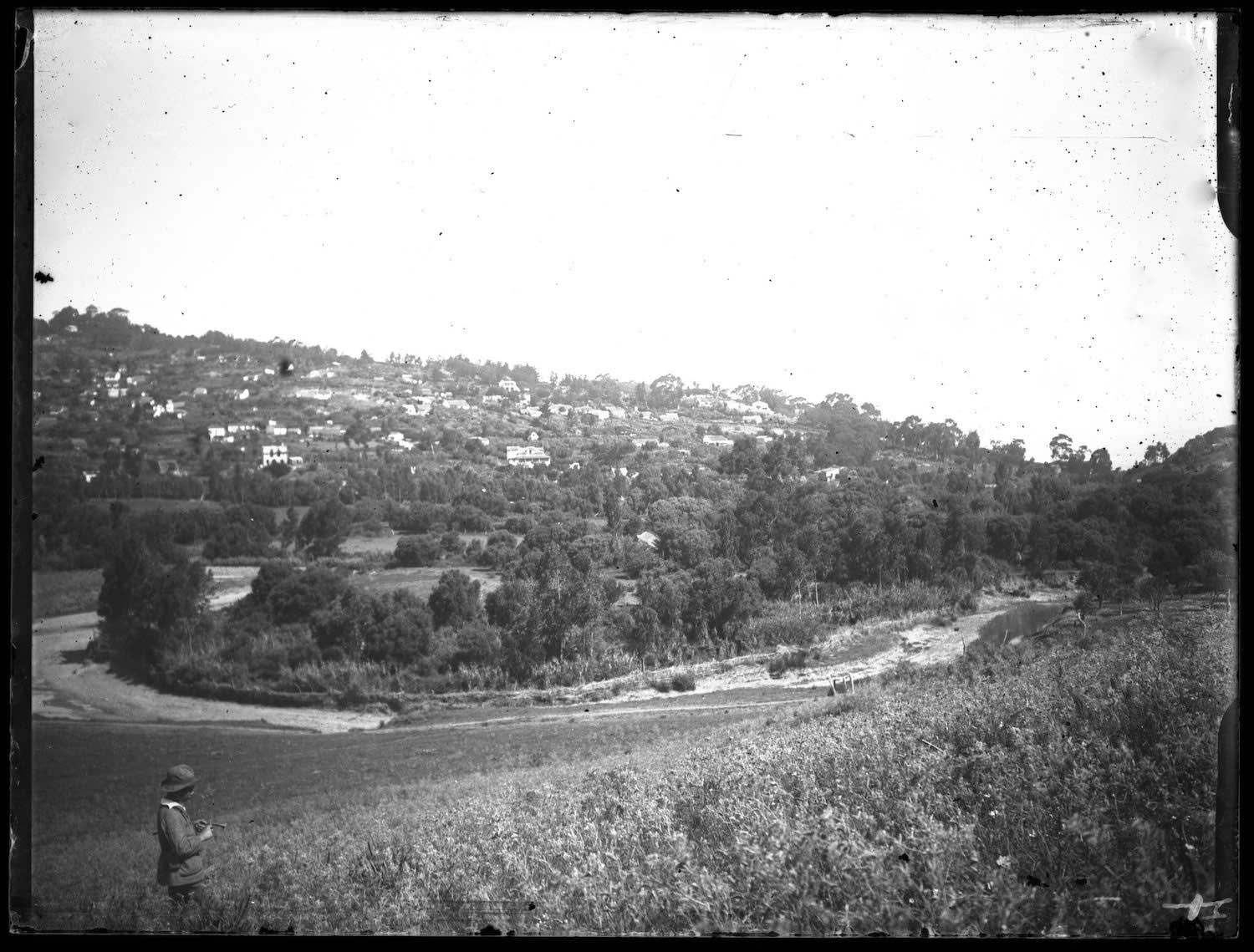 Jews' River looking north; View aceoss the river of residences on the old mountain, a boy in European dress in the foreground