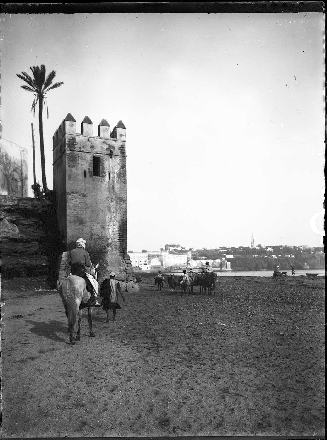 View pedestrians and pack animals on the shoreline passing the city walls