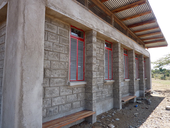 Close-up view of classroom facade, showing operable windows, roof overhang, and shaded area with benches 