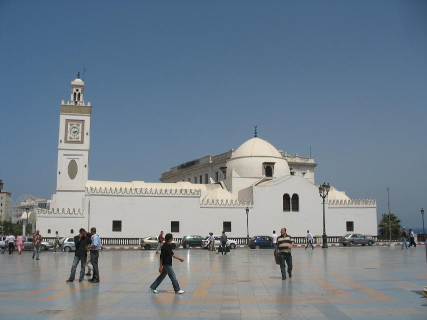 General view of the west elevation of the mosque, looking east from the Place des Martyrs. The principal dome of the mosque appears at center right; the barrel vault roofing the prayer hall runs from the main entrance to the dome