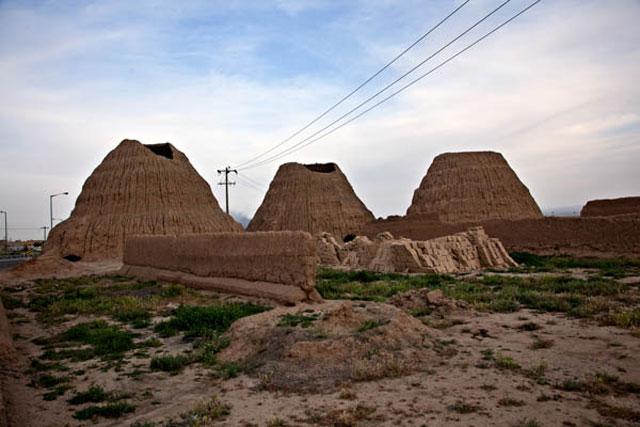 <p>General view of three yakhchals in Sabzavar, showing the mud brick cones and low wall alongside rectangular pools for water</p>