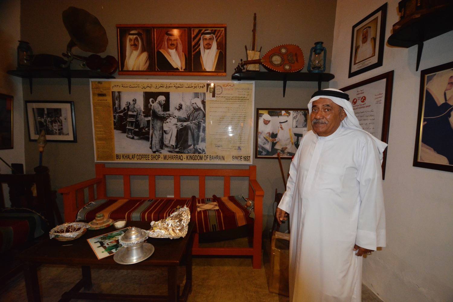 Interior view of the Bu Khalaf Cafe, with the coffee shop's owner standing next to informational sign about the business' history. 