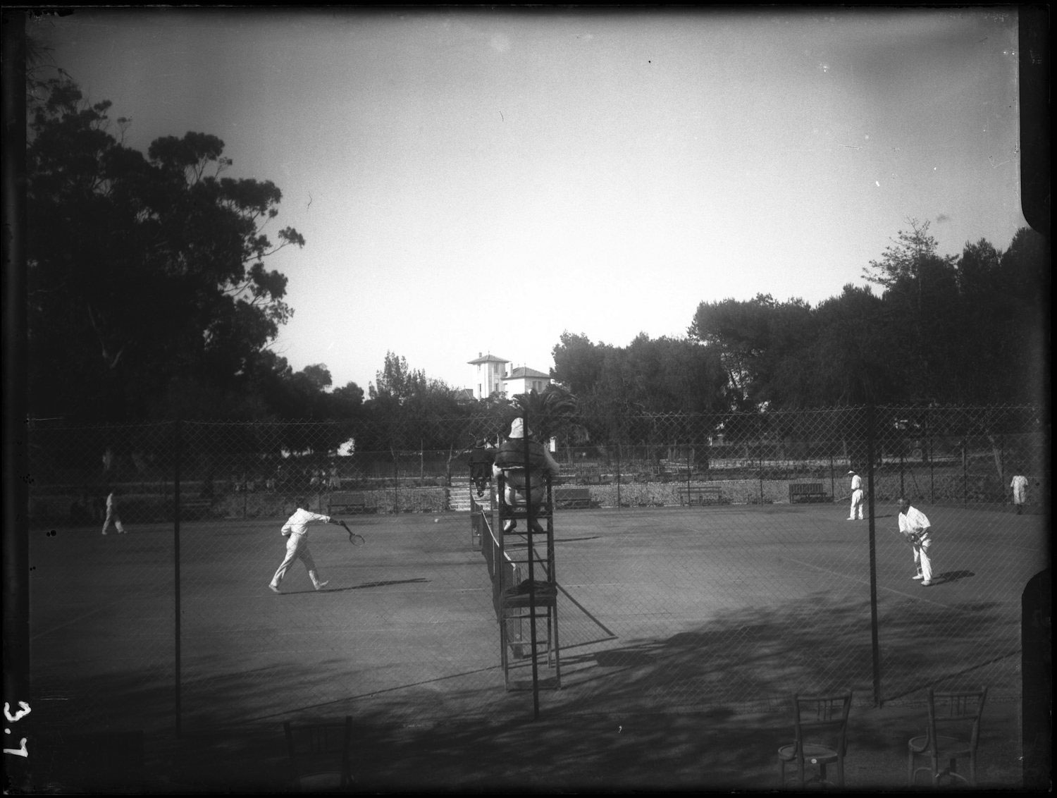 Action shot of a tennis match from outside of the fences of the court.