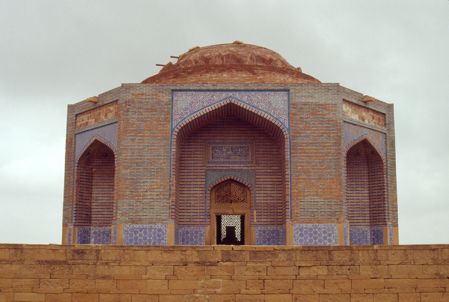 View of tomb from beyond enclosure wall, showing use of glazed blue tiles, enameled bricks and carved sandstone