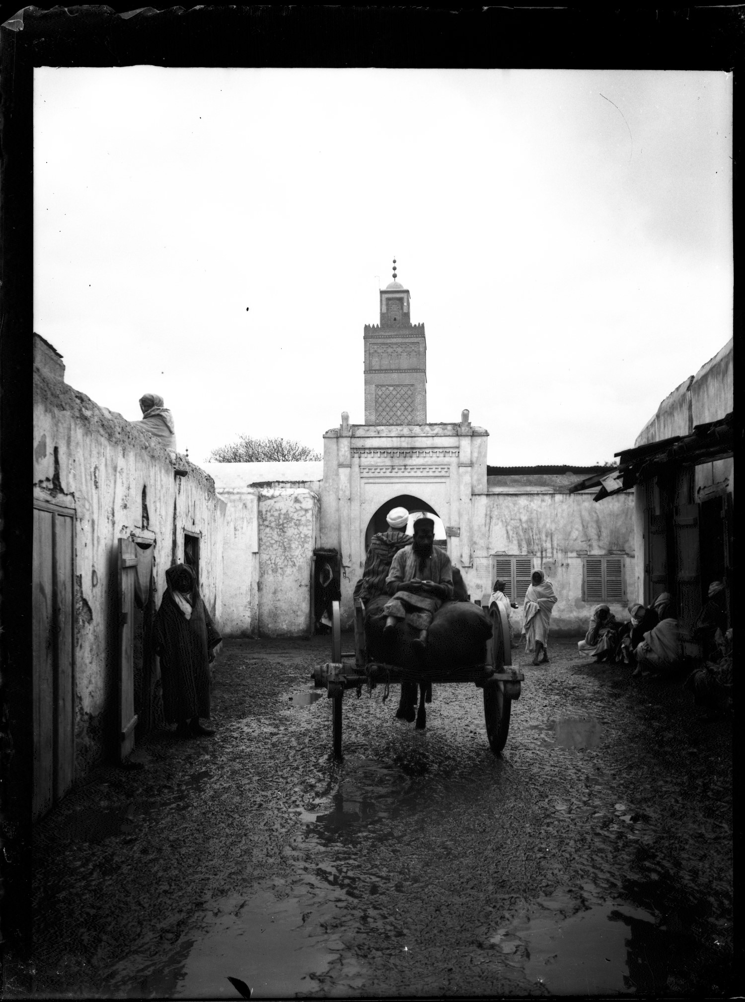 Wagon with people in traditional dress in medina road towards minaret and doorway/gate 